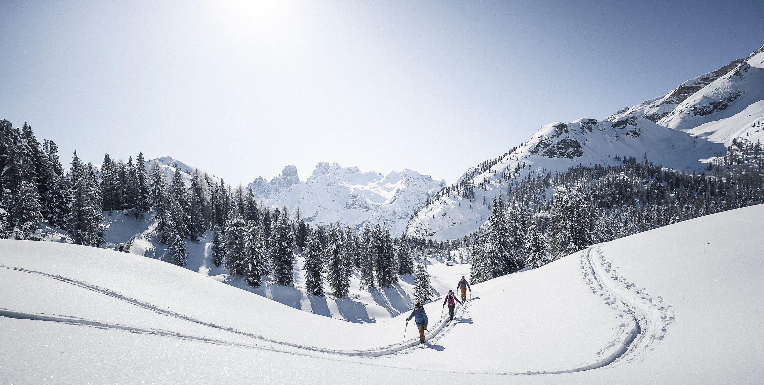 Drei Tourenskigeher*innen in einer verschneiten Berglandschaft.
